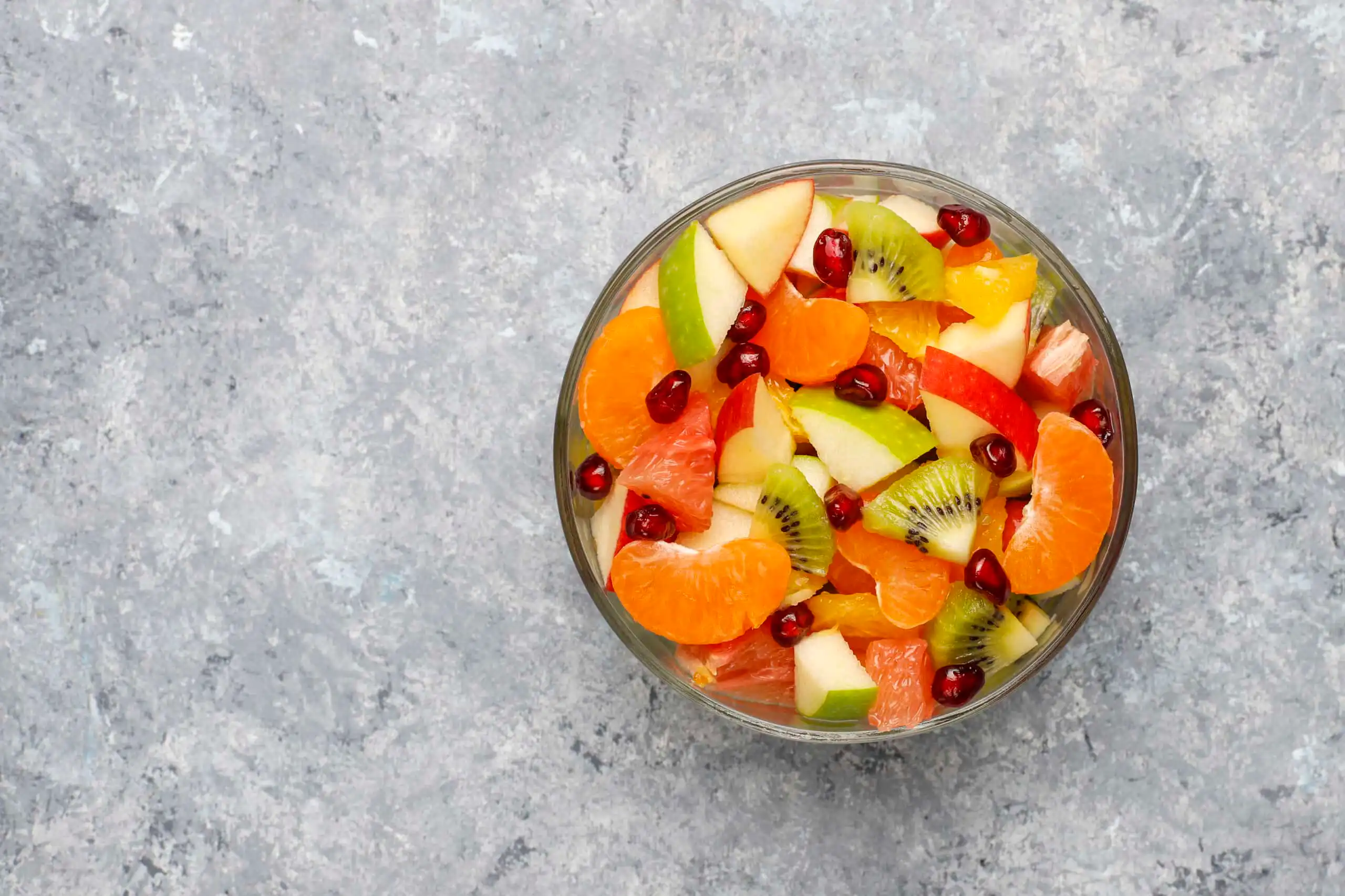 Image of a ceramic bowl filled with fresh fruit, including apples, oranges, and berries, arranged on a kitchen counter.