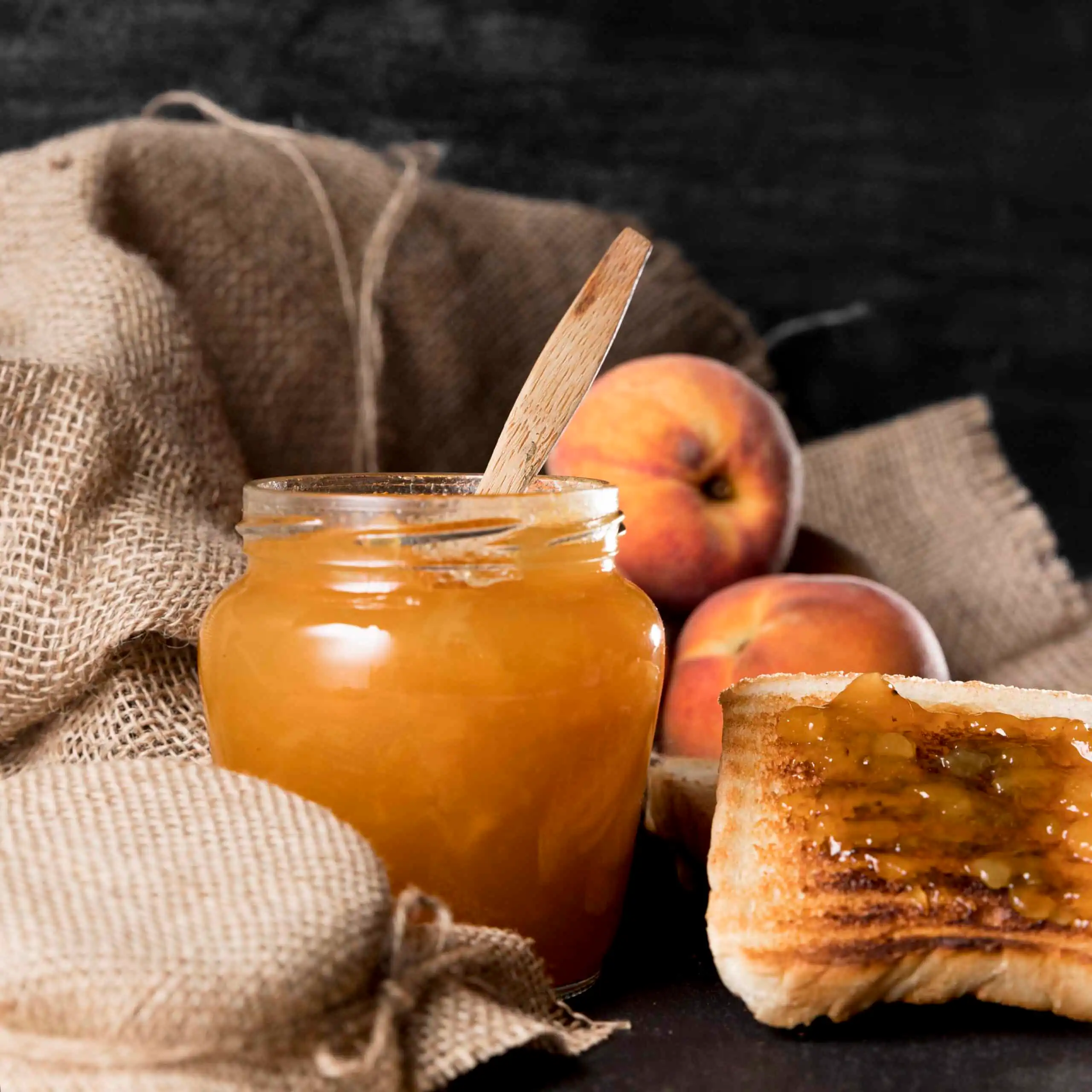 A jar of homemade apple jam with a spreader and fresh apples on a wooden table.
