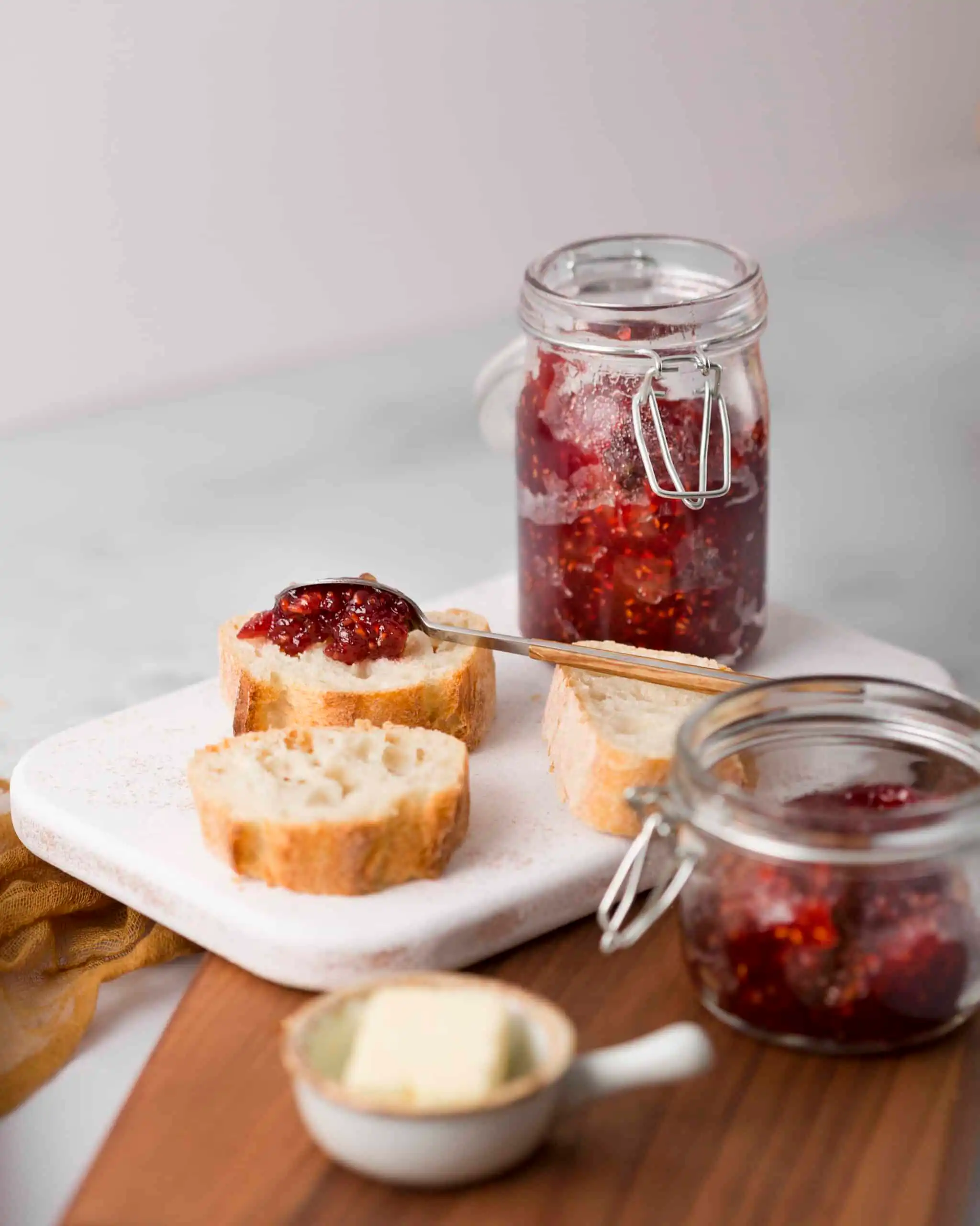 Homemade raspberry jam in a glass jar with fresh raspberries.